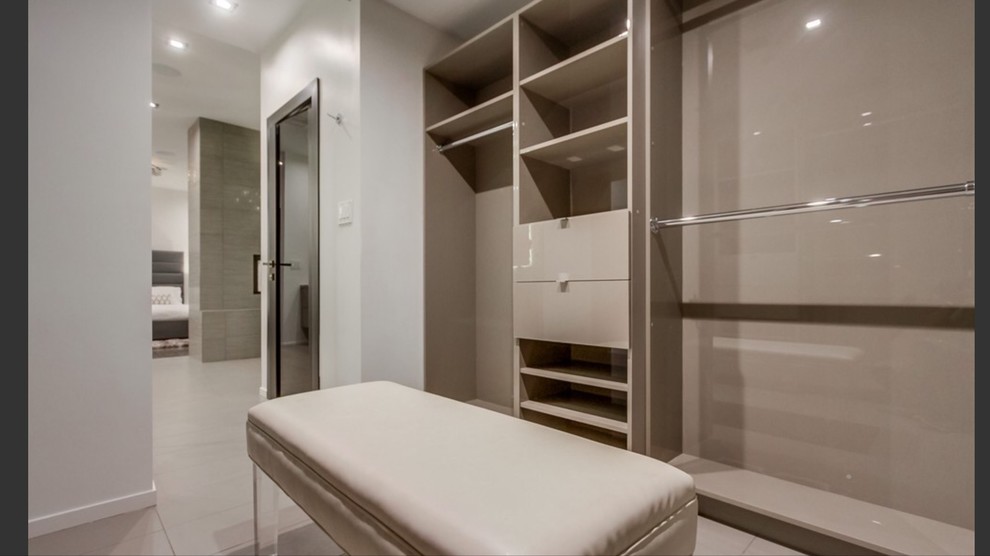 Example of a large minimalist gender-neutral porcelain tile and beige floor walk-in closet design in Los Angeles with flat-panel cabinets and beige cabinets