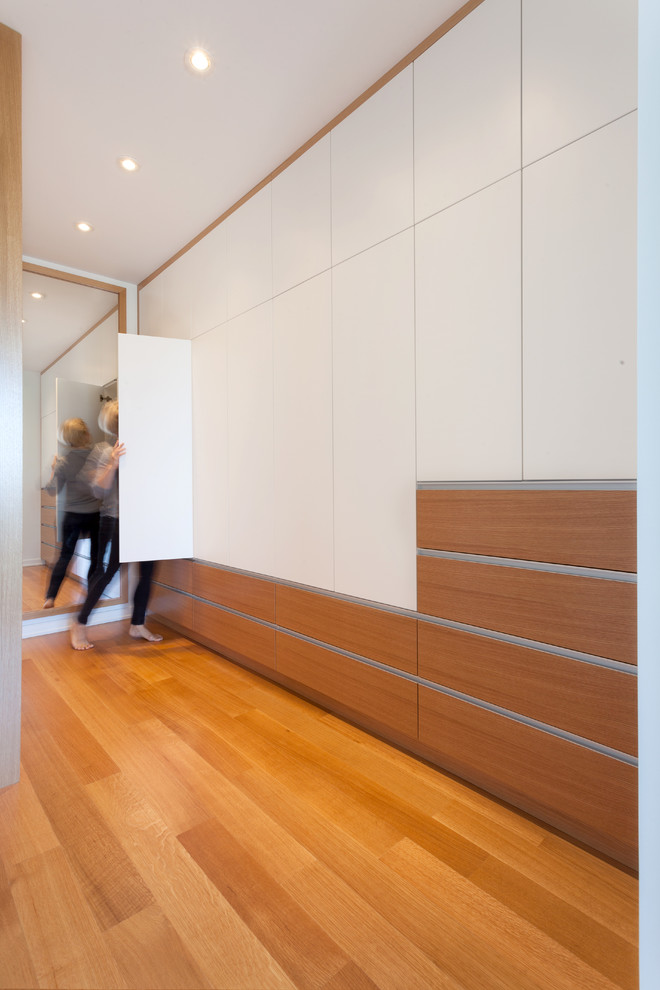 Diseño de armario vestidor unisex minimalista de tamaño medio con armarios con paneles lisos, puertas de armario blancas y suelo de madera clara