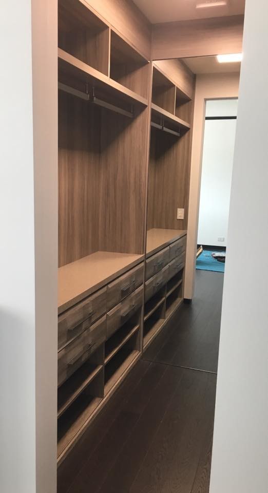 Foto de armario vestidor unisex actual de tamaño medio con armarios con paneles con relieve, puertas de armario de madera oscura, suelo de madera oscura y suelo marrón