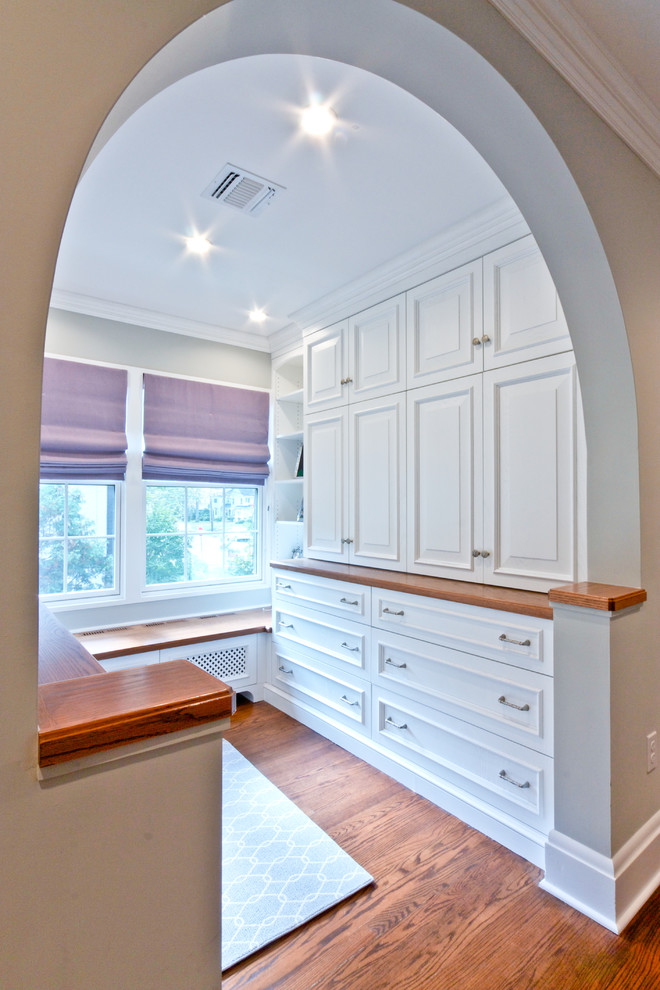 This is an example of a traditional gender neutral walk-in wardrobe in Newark with white cabinets, medium hardwood flooring and raised-panel cabinets.