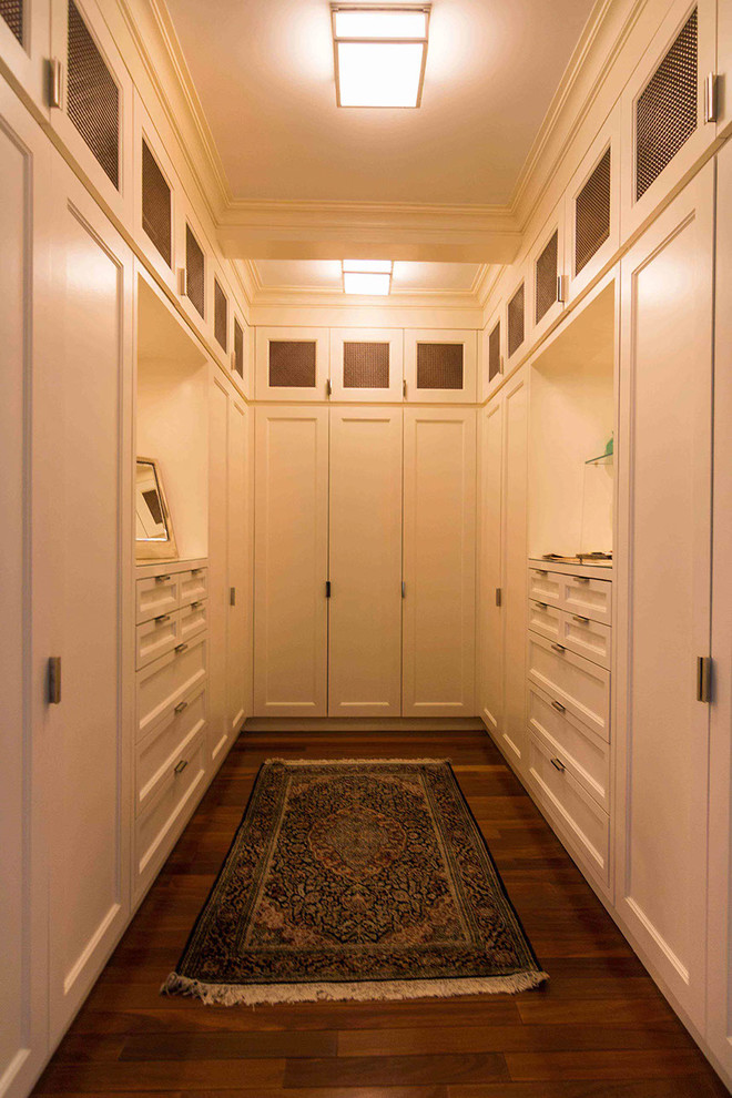 Foto di un'ampia cabina armadio unisex tradizionale con ante in stile shaker, ante bianche, pavimento in legno massello medio e pavimento marrone