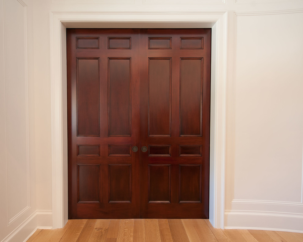 Modelo de armario vestidor clásico grande con armarios con paneles empotrados, puertas de armario de madera en tonos medios y suelo de madera clara