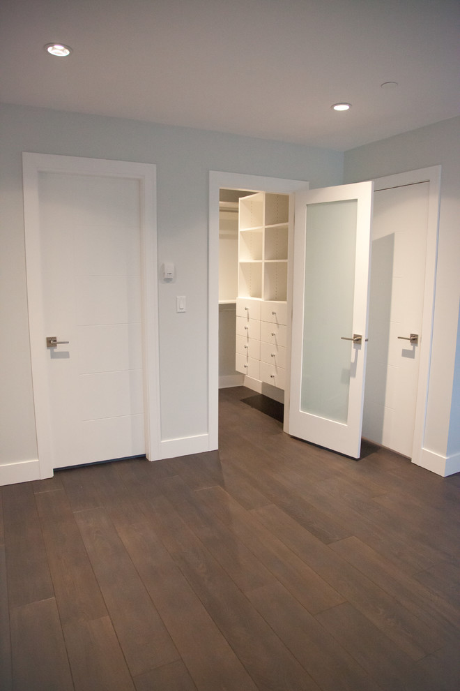 Diseño de armario vestidor unisex minimalista pequeño con armarios con paneles lisos, puertas de armario blancas y suelo de madera oscura