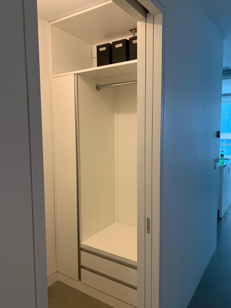 Imagen de armario vestidor industrial pequeño con armarios con paneles lisos, puertas de armario blancas, suelo de cemento y suelo gris