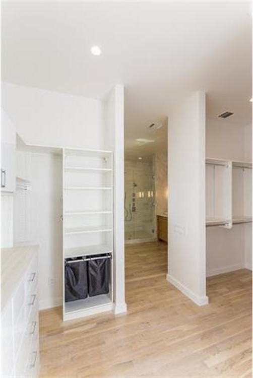 Imagen de armario vestidor unisex clásico grande con armarios abiertos, puertas de armario blancas, suelo de madera clara y suelo beige