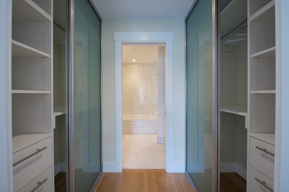 Cette image montre un dressing design de taille moyenne et neutre avec un placard à porte plane, des portes de placard blanches et parquet clair.