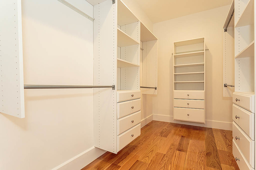 Immagine di una cabina armadio unisex minimalista di medie dimensioni con ante con bugna sagomata, ante bianche e pavimento in legno massello medio