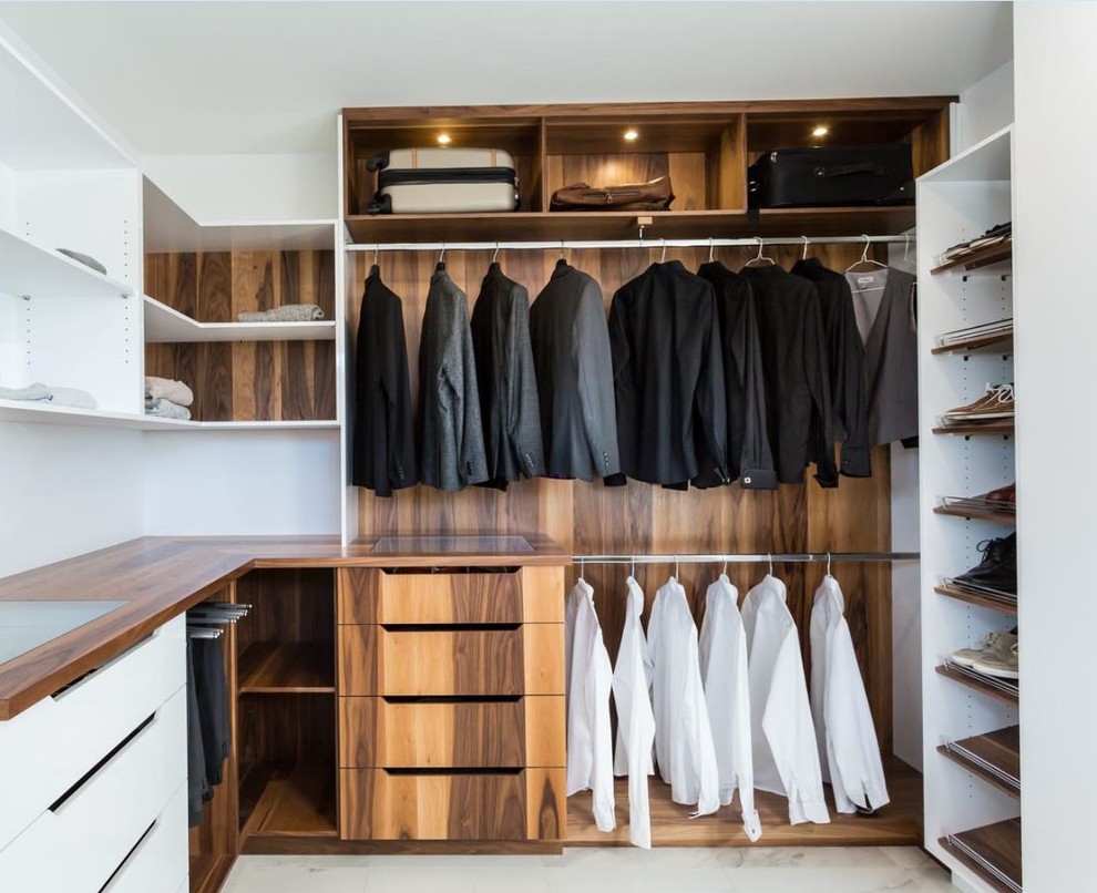 Diseño de armario vestidor unisex minimalista grande con armarios con paneles lisos, puertas de armario de madera oscura, suelo de mármol y suelo blanco