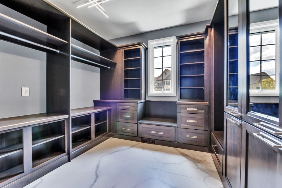 На фото: гардеробная комната унисекс в классическом стиле с темными деревянными фасадами, полом из керамогранита и белым полом с