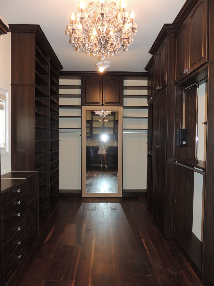 Modelo de armario vestidor unisex tradicional grande con armarios con paneles con relieve, puertas de armario marrones y suelo de madera oscura