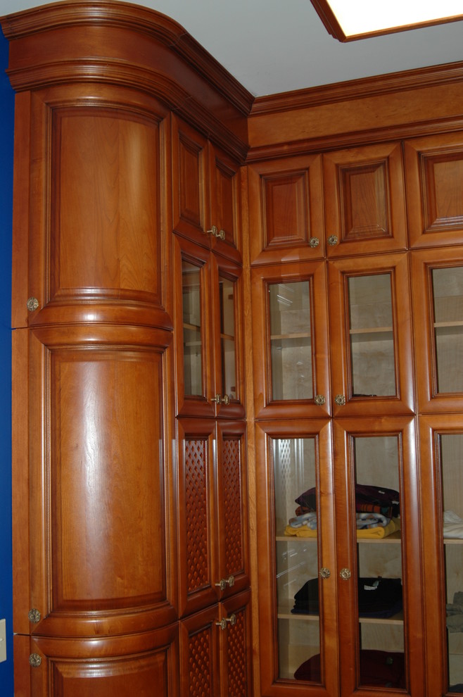 Diseño de armario vestidor unisex tradicional de tamaño medio con armarios con paneles con relieve, puertas de armario de madera clara, suelo de madera oscura y suelo marrón