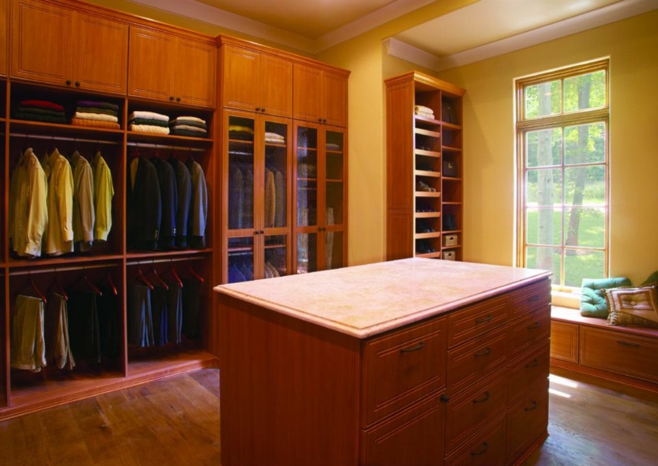 Diseño de armario vestidor unisex clásico con armarios con paneles con relieve, puertas de armario de madera oscura y suelo de madera en tonos medios