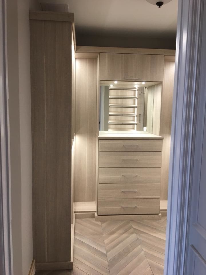 Diseño de armario vestidor unisex actual de tamaño medio con armarios con paneles lisos, puertas de armario de madera oscura, suelo de madera en tonos medios y suelo multicolor