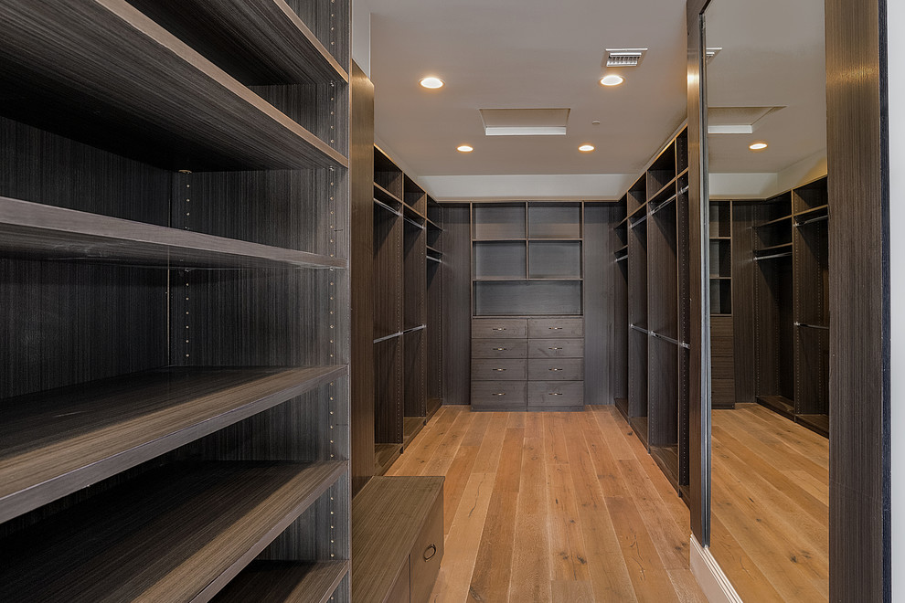 Immagine di una cabina armadio unisex contemporanea di medie dimensioni con ante lisce, ante in legno bruno e pavimento in legno massello medio