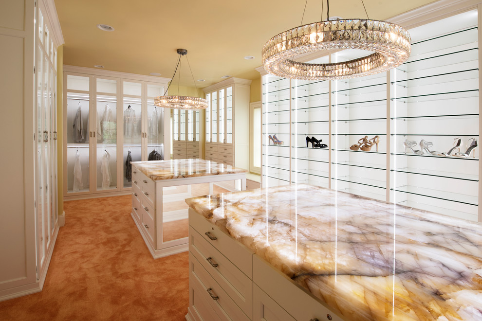 Идея дизайна: огромная гардеробная комната в стиле неоклассика (современная классика) с стеклянными фасадами, белыми фасадами и ковровым покрытием для женщин