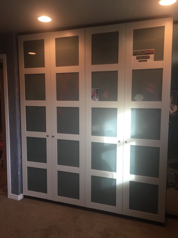 This is an example of a small modern gender neutral standard wardrobe in Denver with glass-front cabinets, white cabinets and carpet.