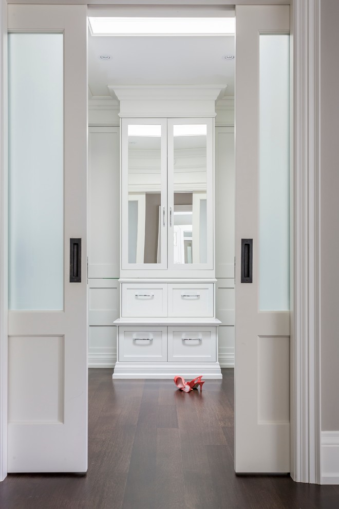 Idée de décoration pour un grand dressing room design neutre avec des portes de placard blanches, parquet foncé et un placard à porte shaker.