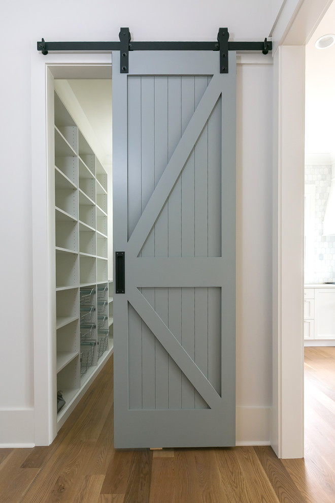 Diseño de armario vestidor unisex costero pequeño con armarios abiertos, puertas de armario blancas, suelo de madera en tonos medios y suelo marrón