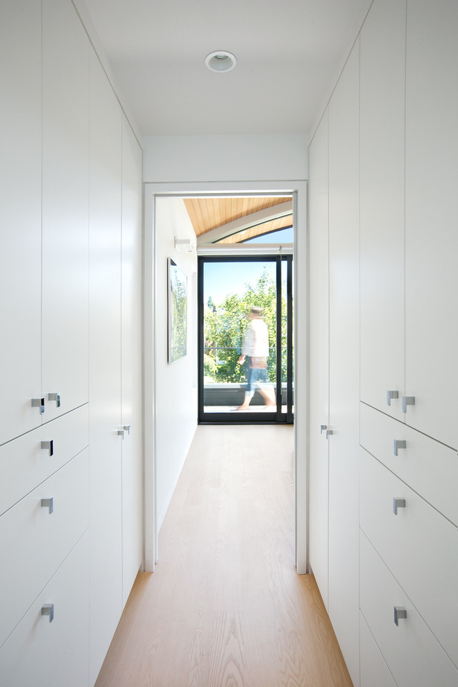 Foto de armario vestidor unisex actual pequeño con armarios con paneles lisos, puertas de armario blancas y suelo de madera clara