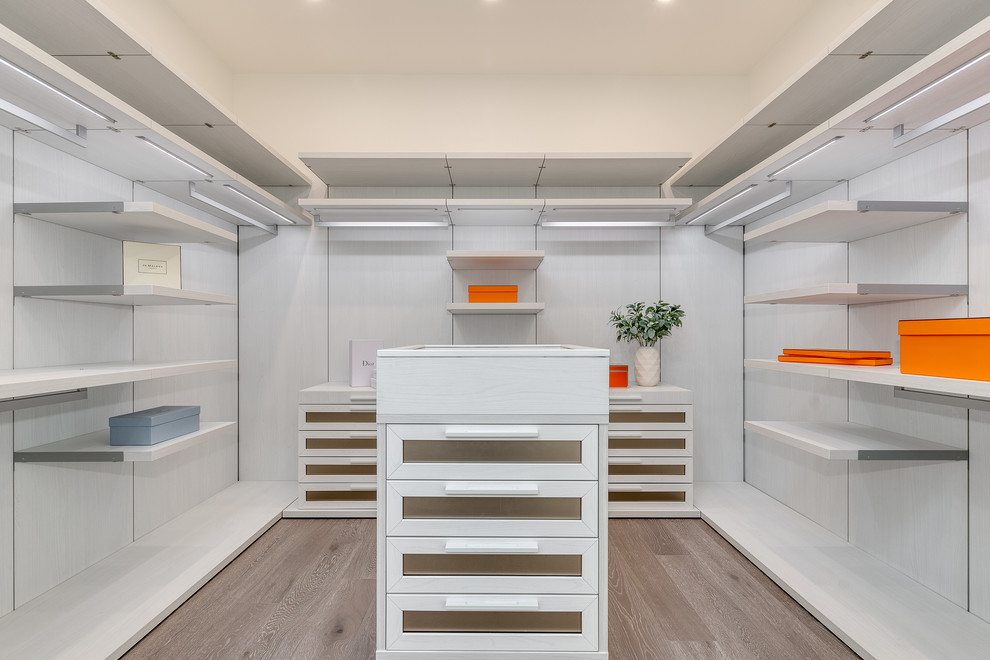 Ejemplo de armario vestidor unisex minimalista grande con armarios estilo shaker, puertas de armario blancas, suelo de madera en tonos medios y suelo marrón