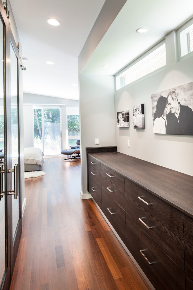 Idée de décoration pour un grand dressing room minimaliste en bois foncé neutre avec un placard à porte plane et un sol en bois brun.
