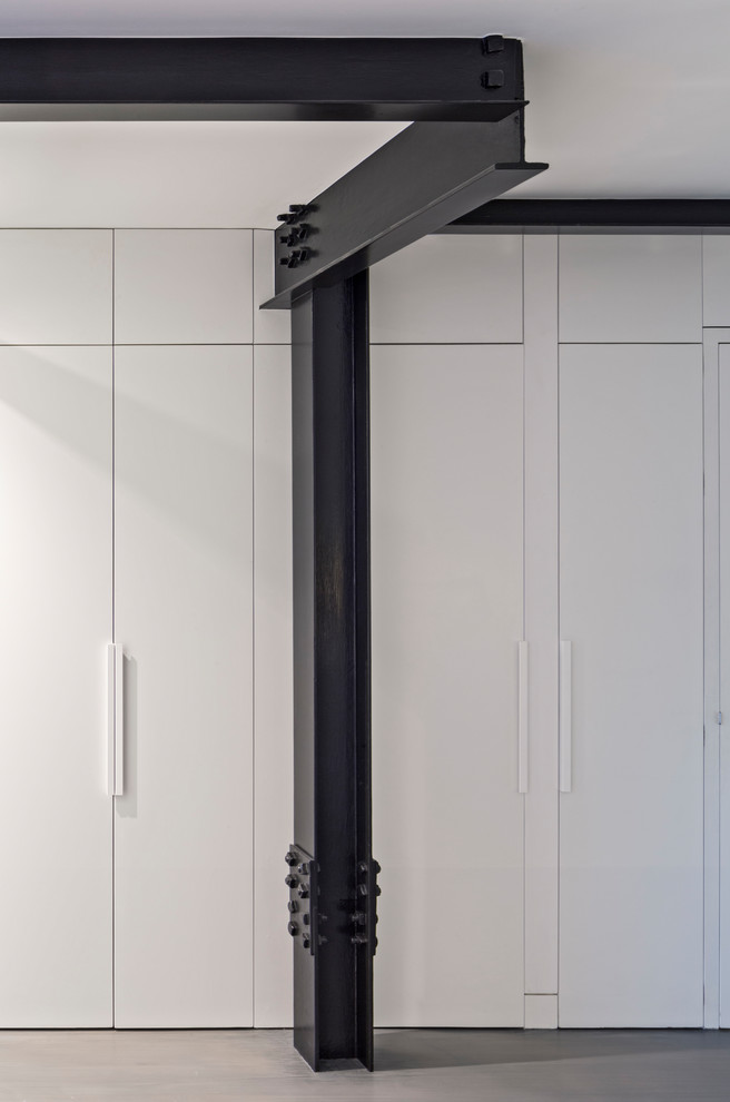 Diseño de armario unisex moderno pequeño con armarios con paneles lisos, puertas de armario blancas, suelo de madera clara y suelo gris