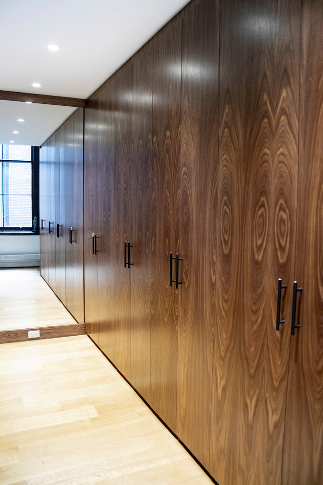 Ejemplo de armario vestidor unisex urbano grande con armarios con paneles lisos, puertas de armario de madera oscura, suelo de madera clara y suelo marrón