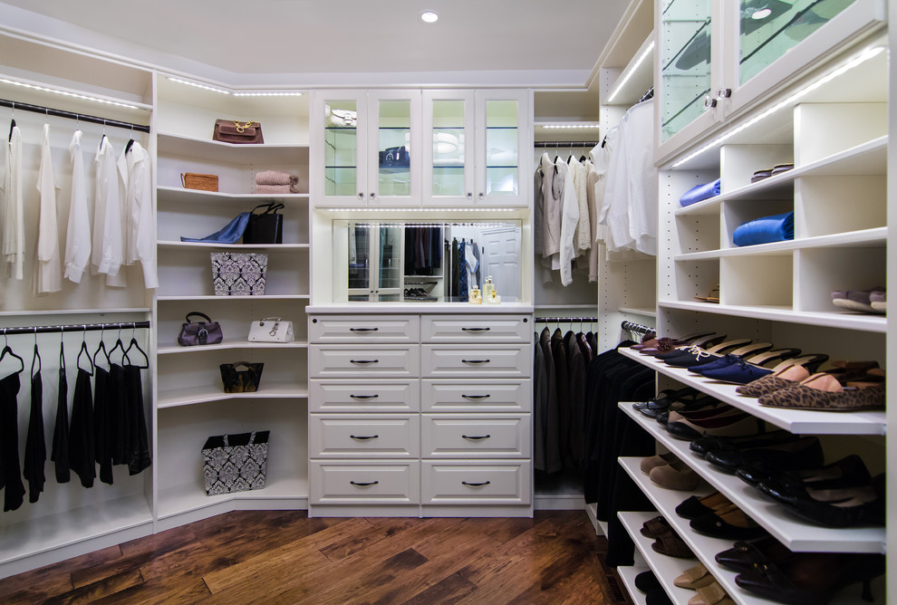 Ejemplo de armario vestidor unisex clásico grande con armarios con paneles con relieve, puertas de armario blancas, suelo de madera en tonos medios y suelo marrón