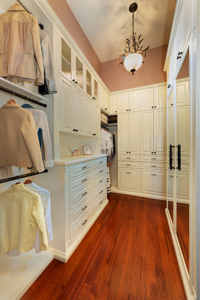 Diseño de armario vestidor de mujer tradicional grande con armarios con paneles con relieve, puertas de armario blancas y suelo de madera en tonos medios