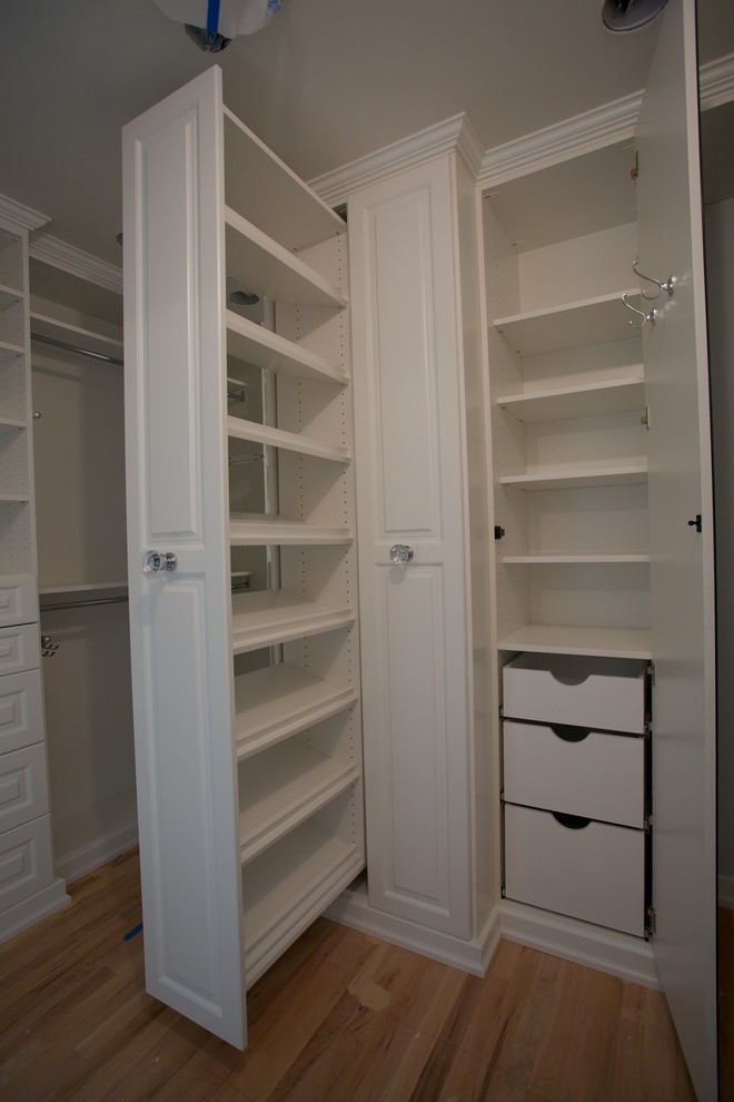 Modelo de armario vestidor unisex tradicional de tamaño medio con armarios abiertos, puertas de armario blancas, suelo de madera clara y suelo marrón