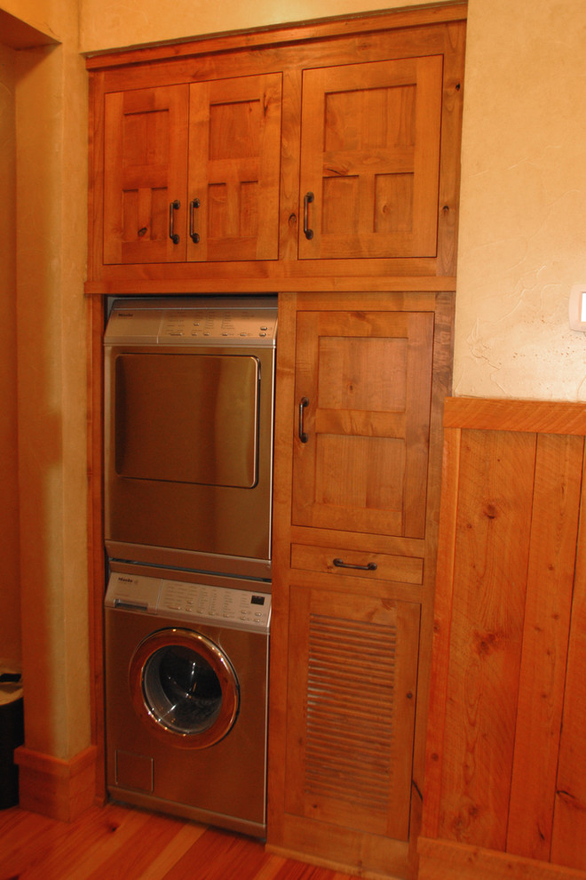 Medium sized rustic single-wall laundry cupboard in Portland with medium wood cabinets, wood worktops, beige walls, medium hardwood flooring, a stacked washer and dryer, brown floors and brown worktops.