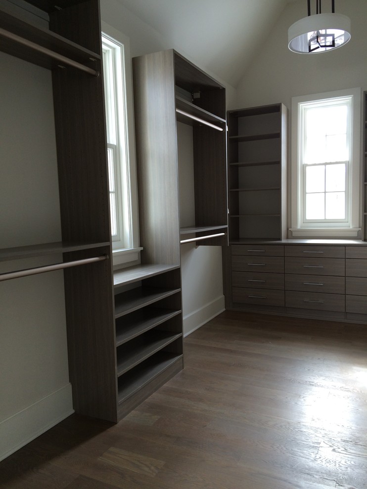 Modelo de armario vestidor unisex de estilo de casa de campo de tamaño medio con armarios con paneles lisos, puertas de armario grises y suelo de madera en tonos medios