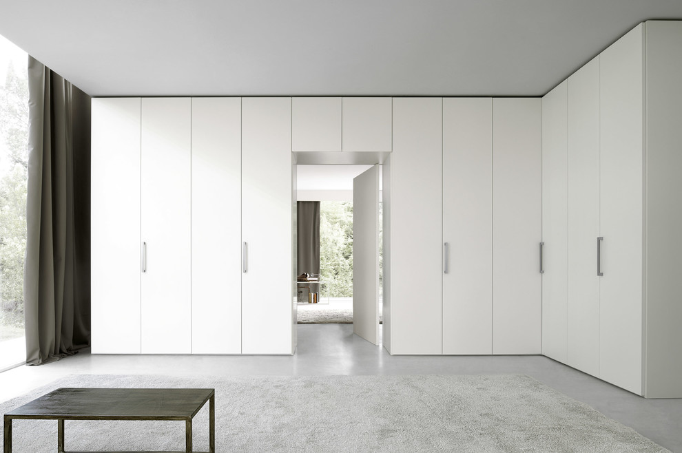 На фото: большой шкаф в нише унисекс в стиле модернизм с плоскими фасадами, белыми фасадами и бетонным полом с