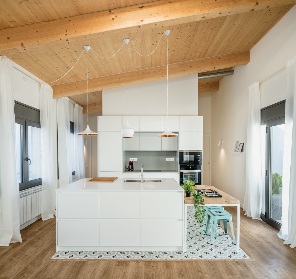 На фото: параллельная кухня-гостиная в скандинавском стиле с врезной мойкой, плоскими фасадами, белыми фасадами, серым фартуком, черной техникой, островом, разноцветным полом, белой столешницей и красивой плиткой с