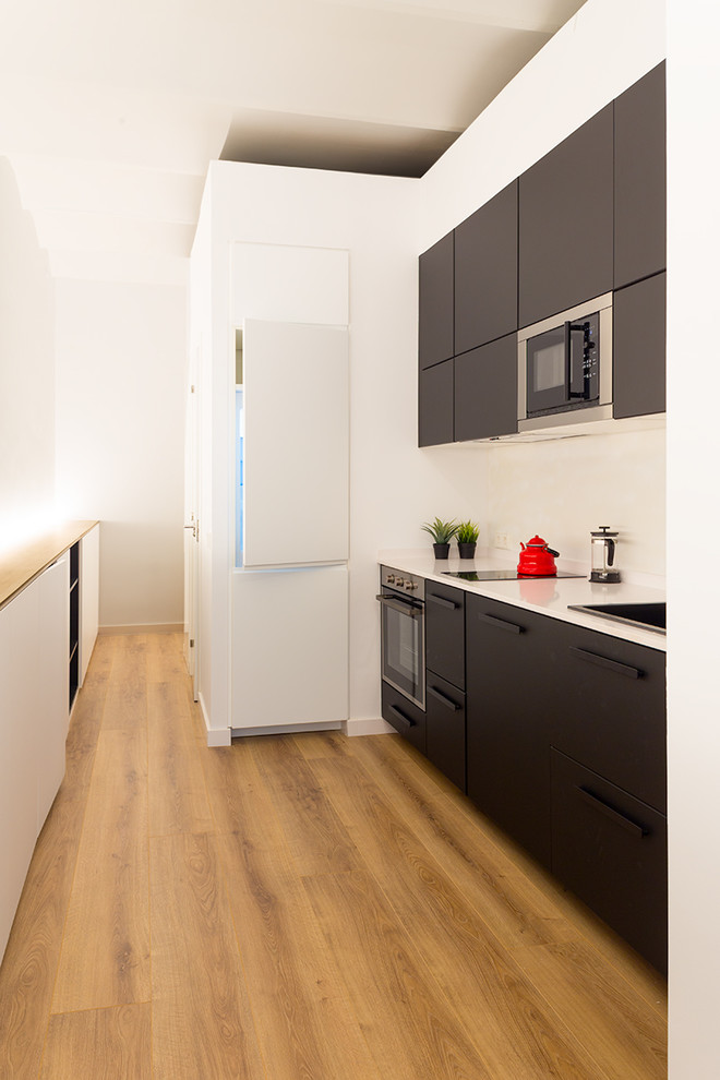 Idéer för små funkis linjära vitt kök med öppen planlösning, med släta luckor, svarta skåp, vitt stänkskydd, mellanmörkt trägolv, brunt golv, en enkel diskho och integrerade vitvaror