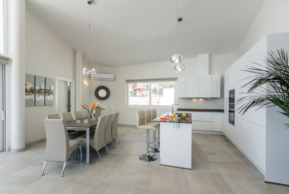 Example of a trendy l-shaped gray floor eat-in kitchen design in Other with flat-panel cabinets, white cabinets, black appliances, an island, an undermount sink, gray backsplash, glass sheet backsplash and black countertops