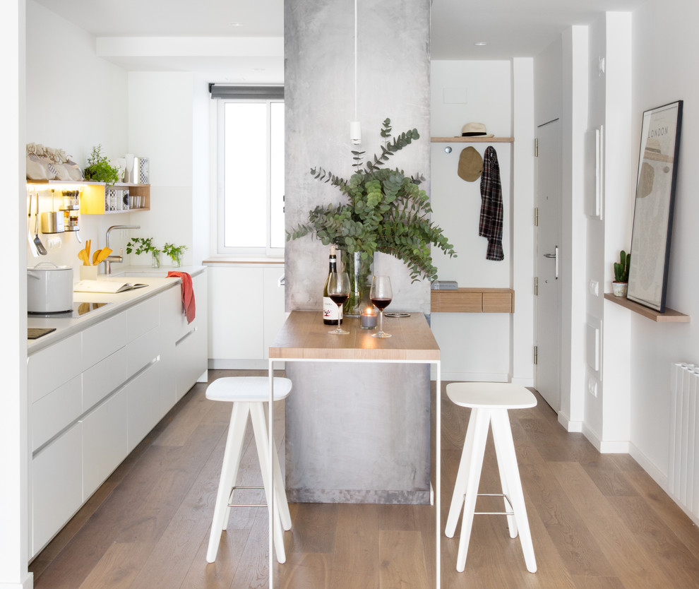 Einzeilige, Kleine Skandinavische Küche mit Unterbauwaschbecken, flächenbündigen Schrankfronten, weißen Schränken, braunem Holzboden, Halbinsel und Küchenrückwand in Weiß in Barcelona