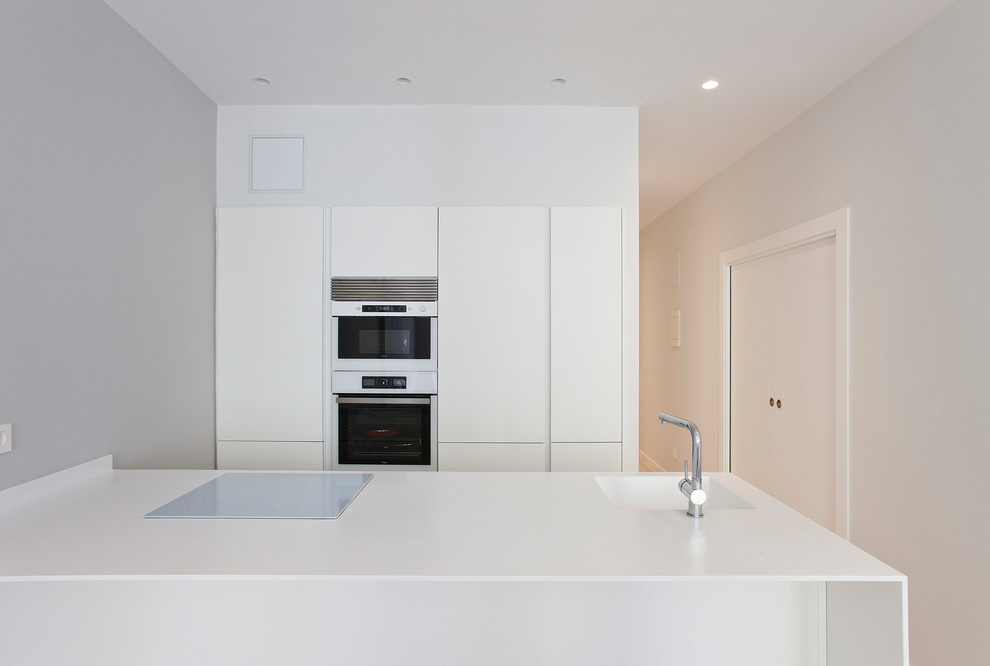 Cette photo montre une cuisine ouverte linéaire tendance de taille moyenne avec un évier intégré, un placard à porte plane, des portes de placard blanches, un électroménager blanc et une péninsule.