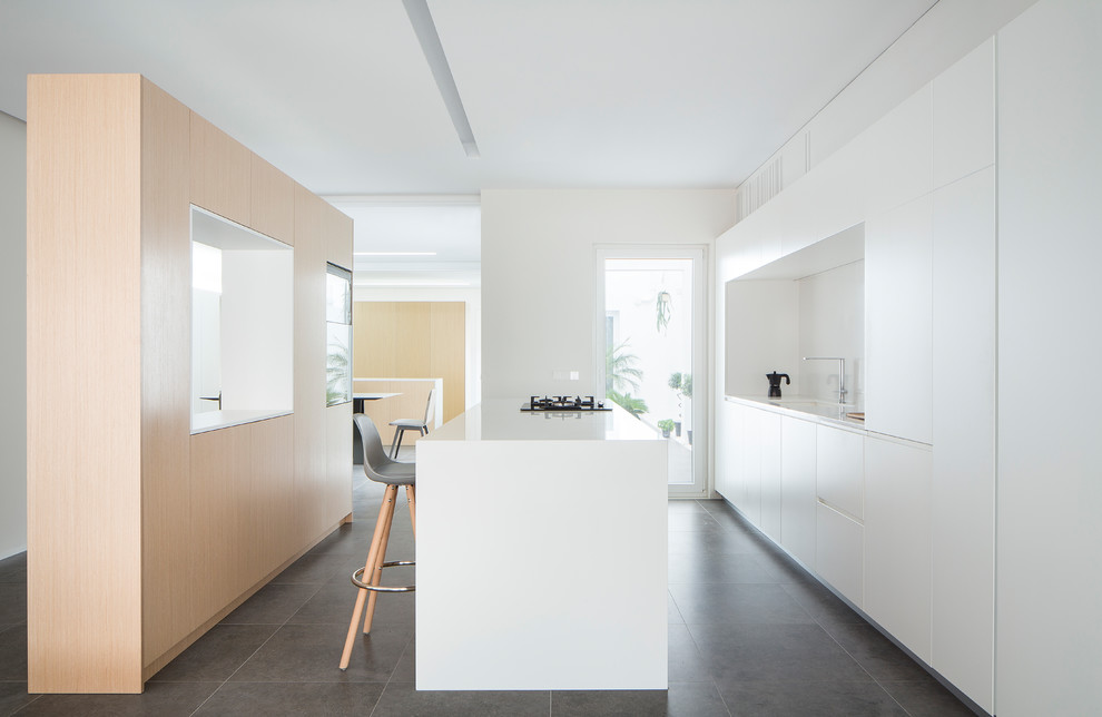 Zweizeilige Moderne Wohnküche mit flächenbündigen Schrankfronten, weißen Schränken, Kücheninsel, Unterbauwaschbecken, Küchenrückwand in Weiß, Elektrogeräten mit Frontblende, grauem Boden und weißer Arbeitsplatte in Valencia