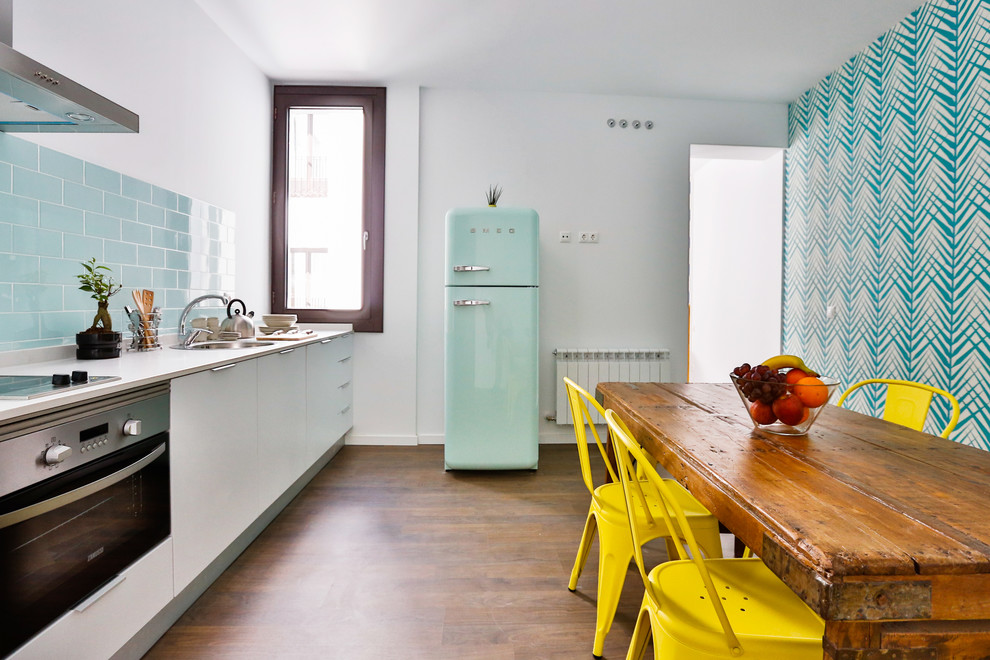 Einzeilige, Mittelgroße Moderne Wohnküche ohne Insel mit Waschbecken, flächenbündigen Schrankfronten, weißen Schränken, Küchenrückwand in Blau, Rückwand aus Keramikfliesen, bunten Elektrogeräten und dunklem Holzboden in Madrid