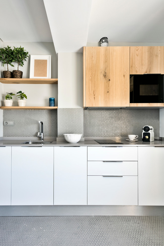 Immagine di una cucina lineare design di medie dimensioni con lavello sottopiano, ante lisce, ante bianche, paraspruzzi grigio, paraspruzzi con piastrelle a mosaico, elettrodomestici neri e top grigio