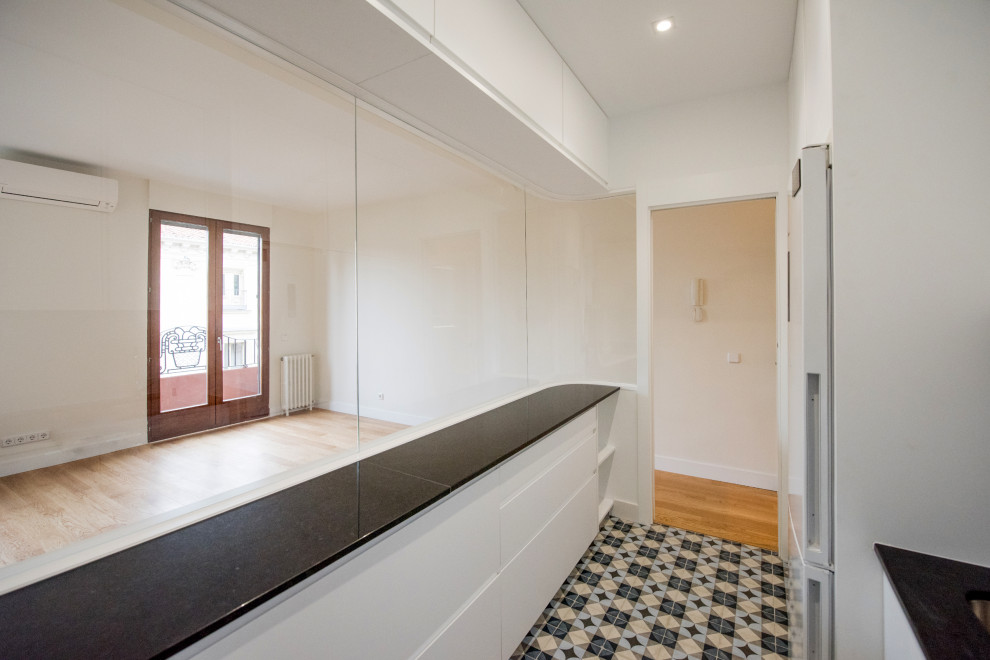 Small modern u-shaped enclosed kitchen in Other with a submerged sink, flat-panel cabinets, white cabinets, granite worktops, white splashback, ceramic splashback, white appliances, ceramic flooring, no island, blue floors and black worktops.