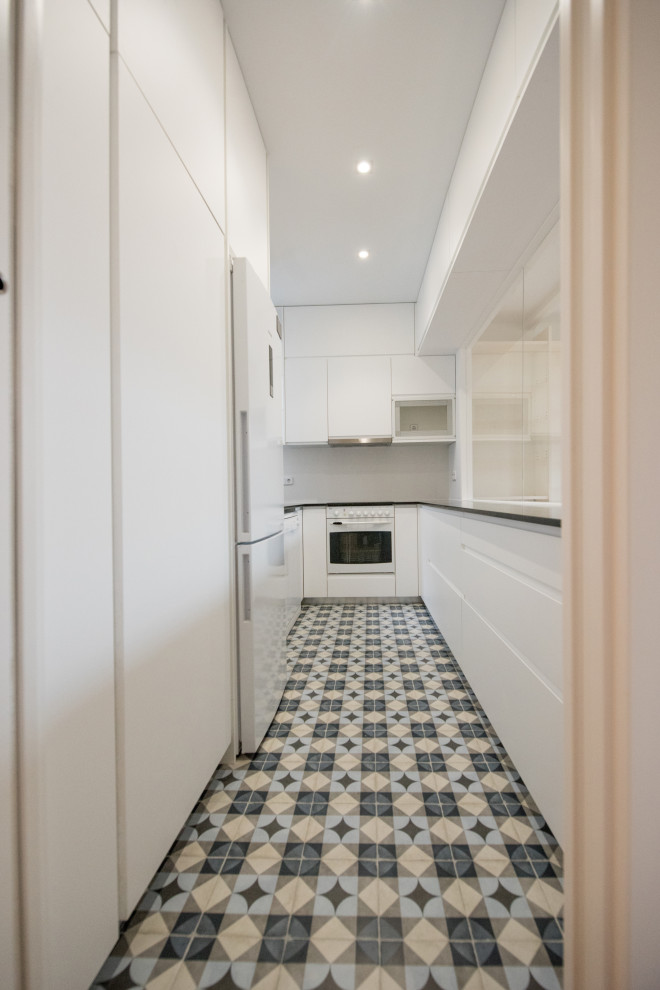 This is an example of a small modern u-shaped enclosed kitchen in Other with a submerged sink, flat-panel cabinets, white cabinets, granite worktops, white splashback, ceramic splashback, white appliances, ceramic flooring, no island, blue floors and black worktops.