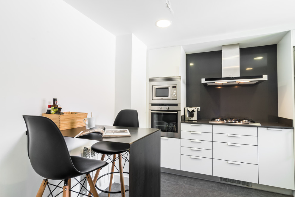 Modern inredning av ett litet linjärt kök och matrum, med släta luckor, vita skåp, svart stänkskydd, rostfria vitvaror och grått golv