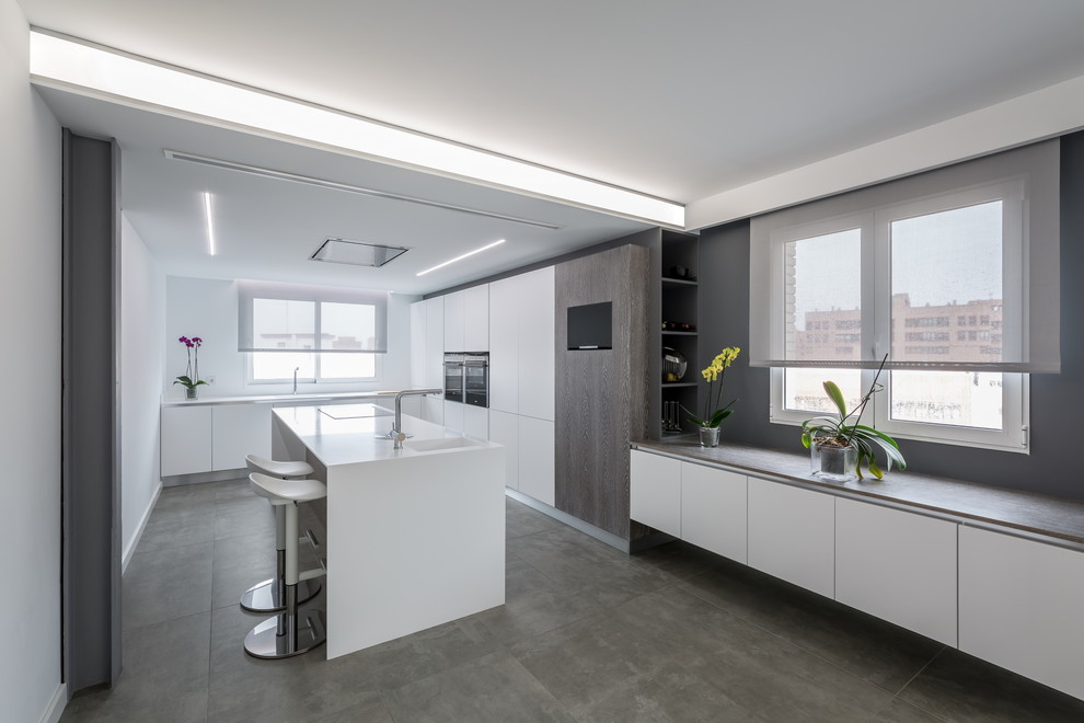 Photo of a large contemporary grey and white enclosed kitchen in Valencia with an integrated sink, flat-panel cabinets, white cabinets, an island, composite countertops, stainless steel appliances and concrete flooring.
