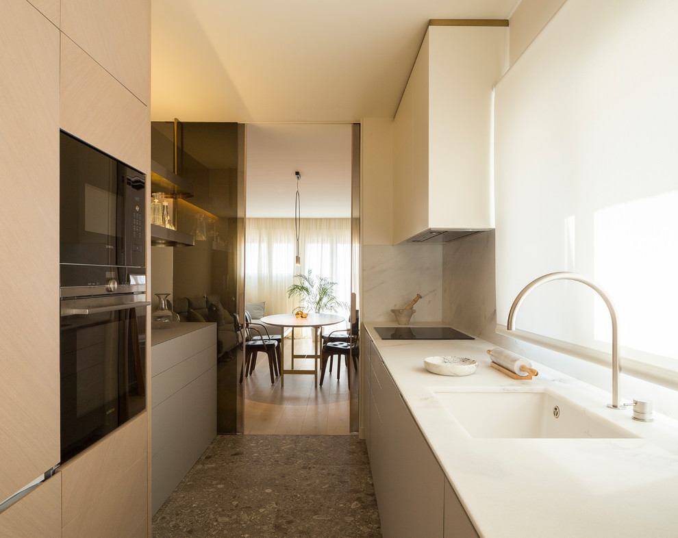 Inspiration for a mid-sized contemporary galley gray floor enclosed kitchen remodel in Valencia with an undermount sink, flat-panel cabinets, beige cabinets, marble countertops, white backsplash, marble backsplash, black appliances and no island