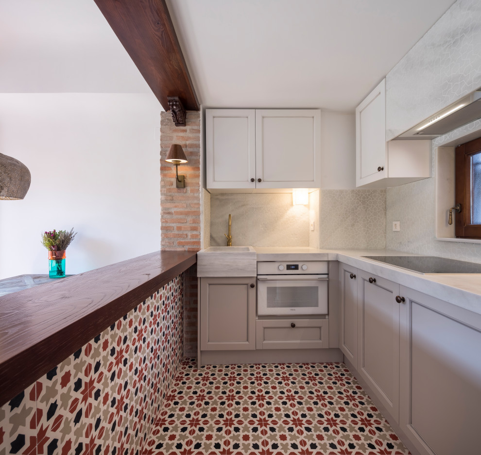 Inspiration for a small mediterranean l-shaped open plan kitchen in Other with a belfast sink, white cabinets, marble worktops, marble splashback, white appliances, ceramic flooring, no island, red floors and white worktops.