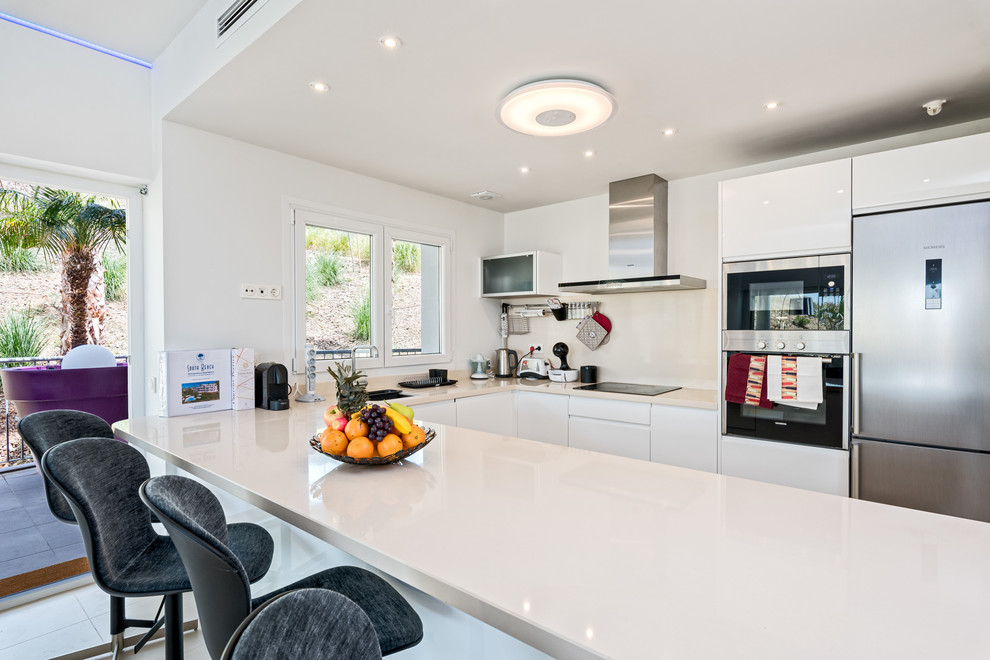 Large danish u-shaped open concept kitchen photo in Malaga with a single-bowl sink, flat-panel cabinets, white cabinets, white backsplash, stainless steel appliances and a peninsula
