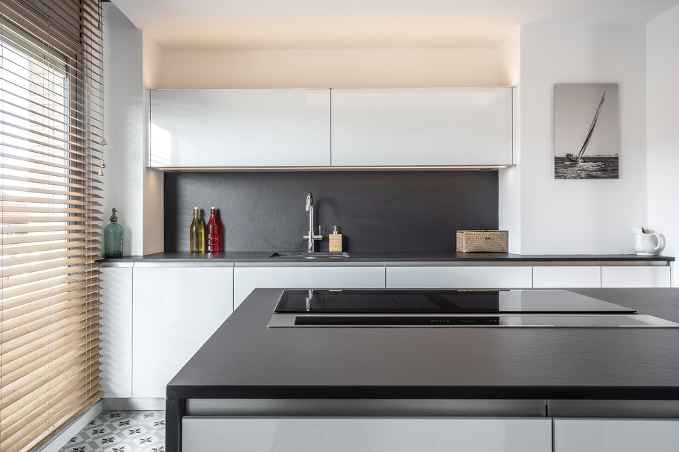 Inspiration for a large scandinavian open plan kitchen in Barcelona with a submerged sink, flat-panel cabinets, white cabinets, engineered stone countertops, black splashback, integrated appliances, cement flooring, an island, multi-coloured floors and black worktops.