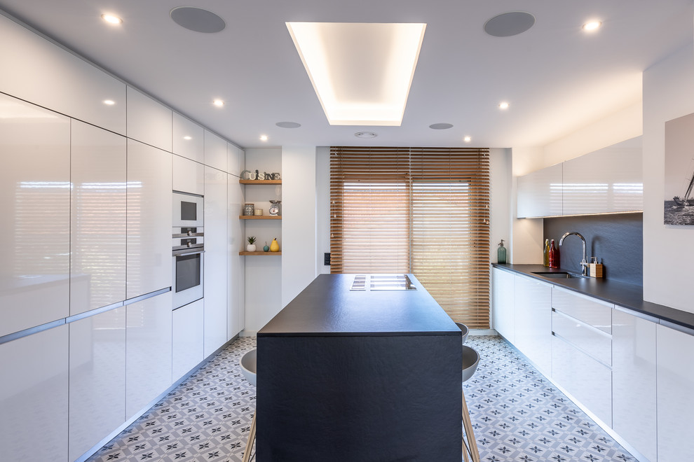 This is an example of a large scandi kitchen in Barcelona with a submerged sink, flat-panel cabinets, white cabinets, engineered stone countertops, black splashback, integrated appliances, cement flooring, an island, multi-coloured floors and black worktops.